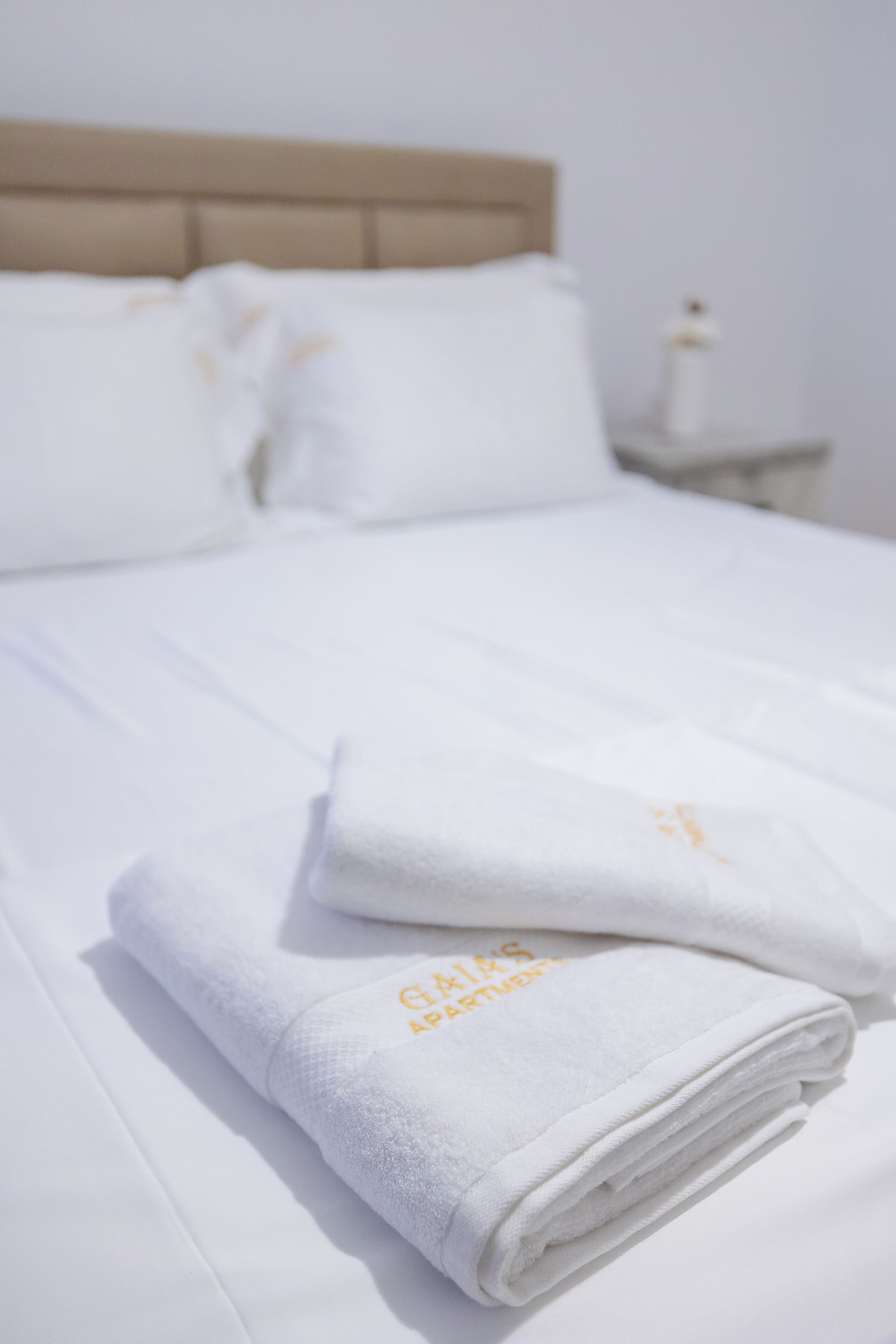 A neatly made bed with white linens and a folded towel with a logo.