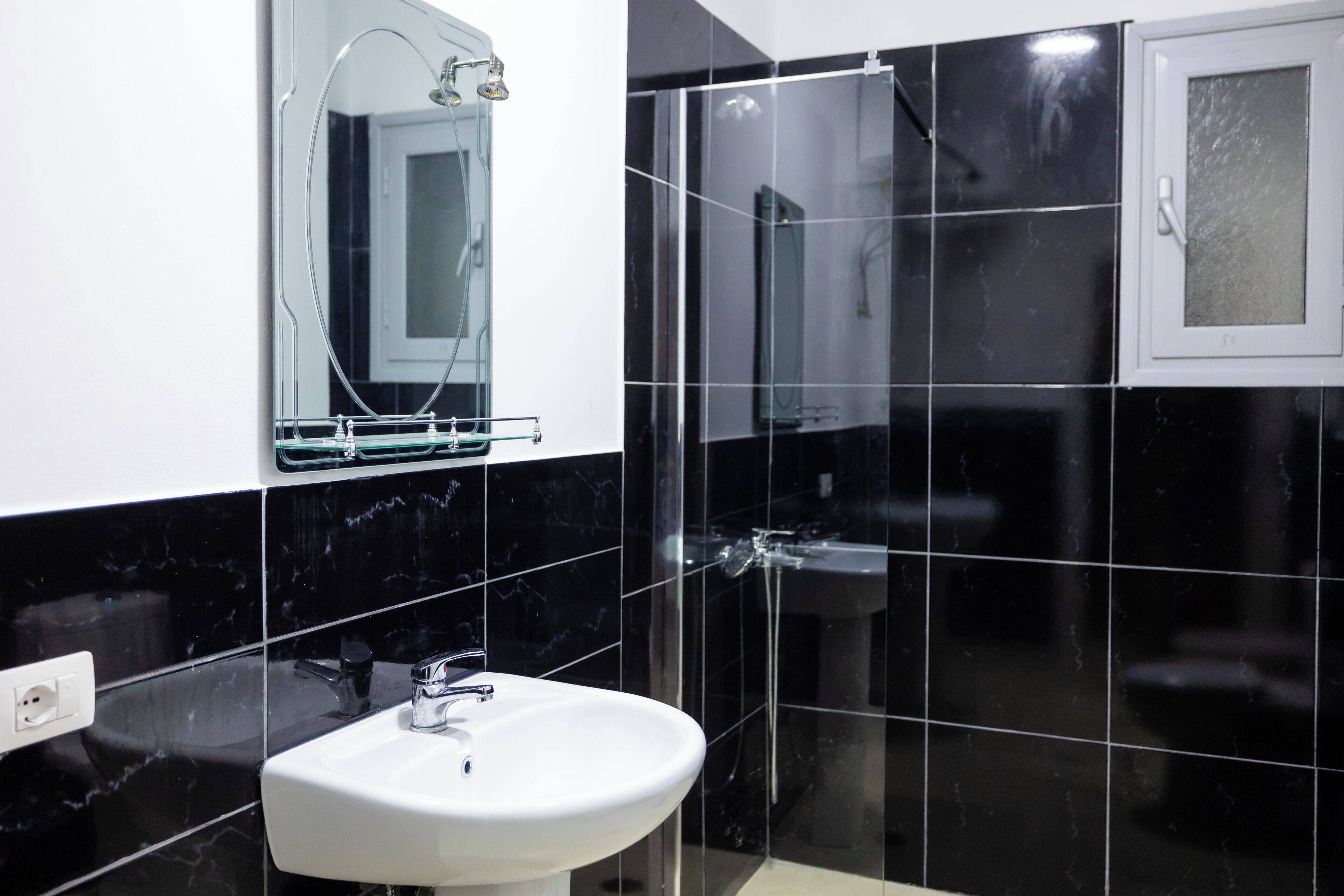 Un bagno con un lavandino bianco, uno specchio e pareti rivestite di piastrelle nere.