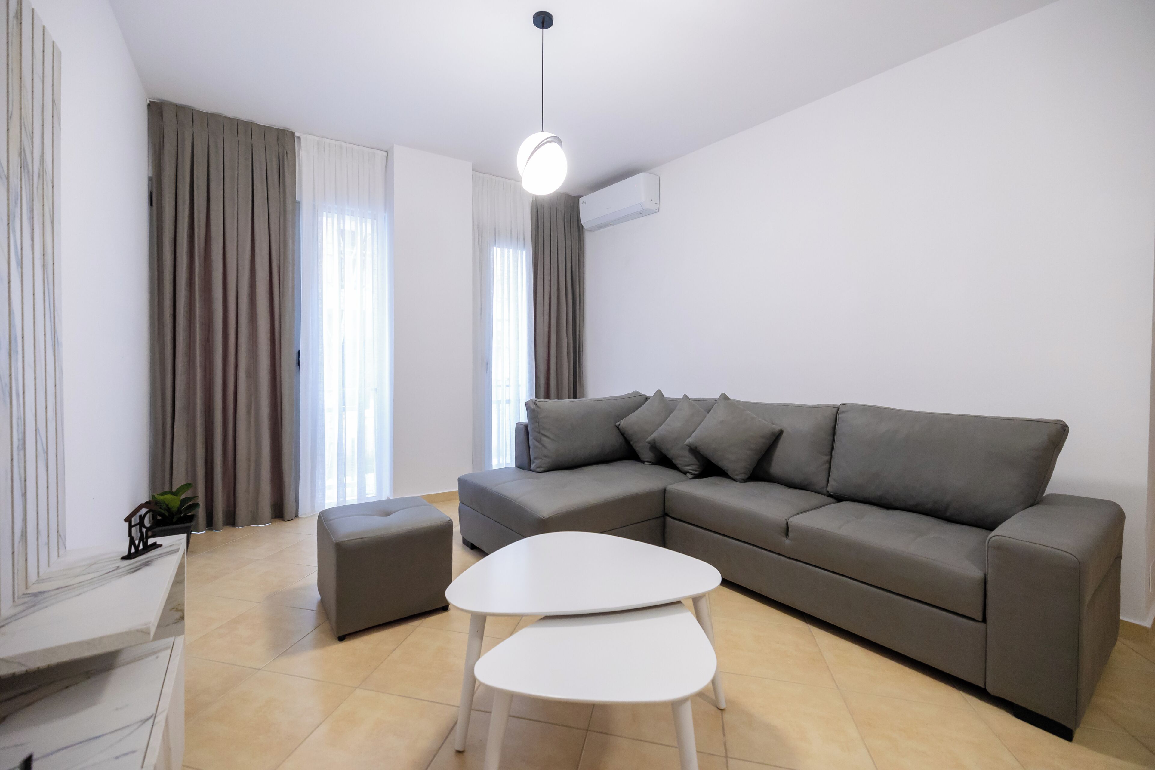 Una sala moderna con un sofá seccional gris, una mesa de centro blanca y una escalera de mármol.