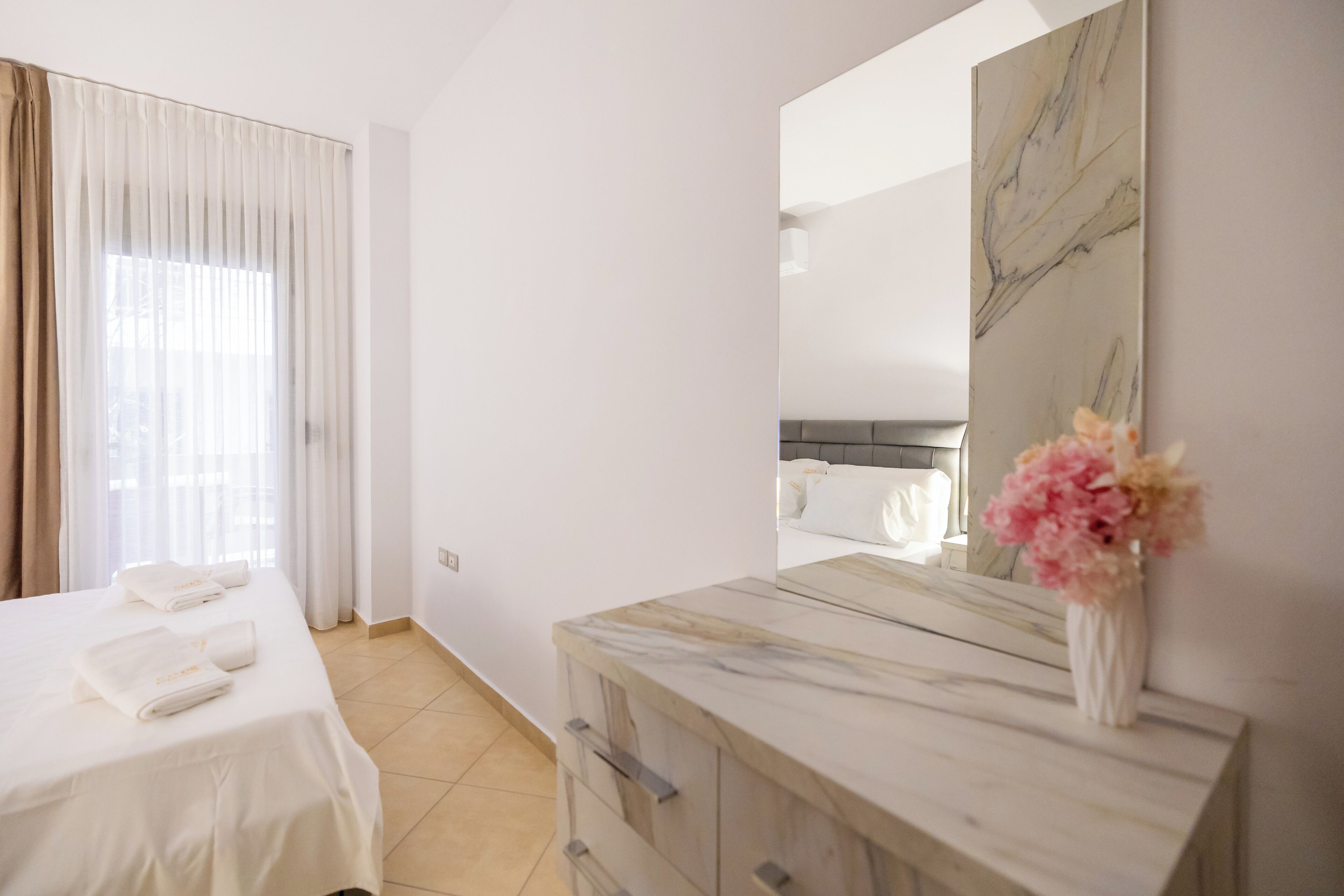 Ein Hotelzimmer mit Bett, Schminktisch, Spiegel und einer Blumenvase.
