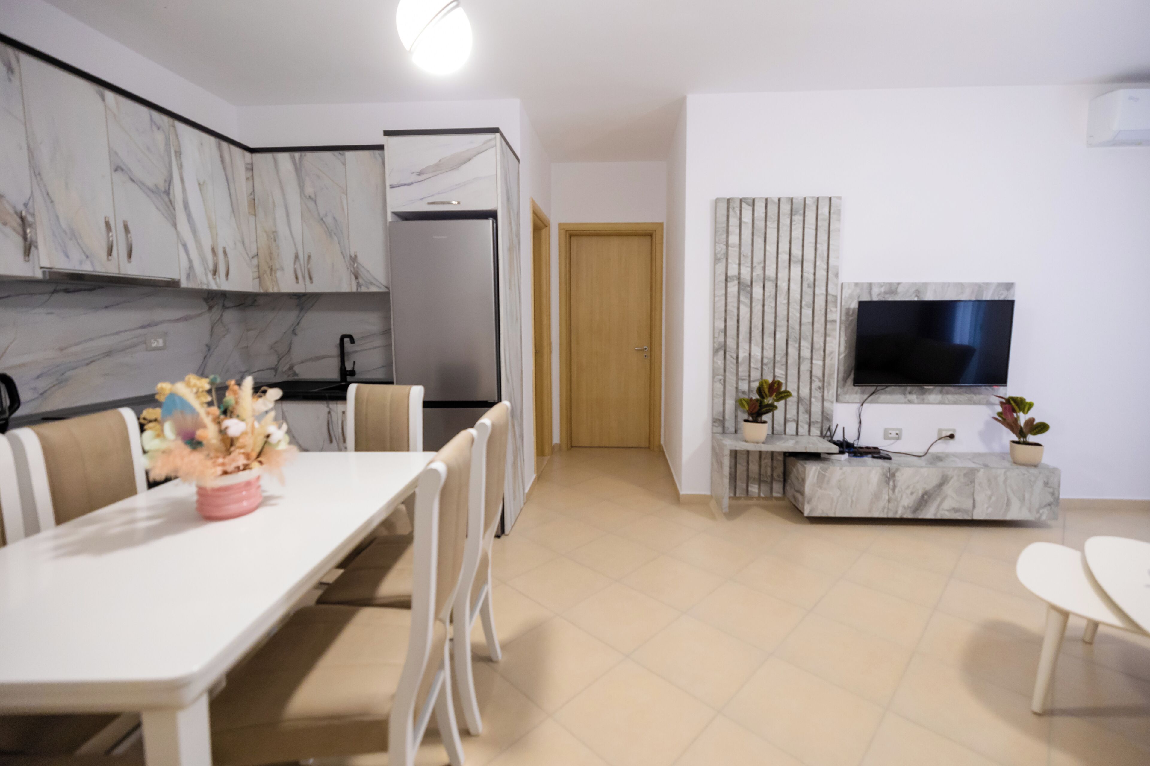 Eine moderne Küche mit Marmor-Schränken, einem eingebauten Kühlschrank und einem Essbereich mit weißem Tisch und Stühlen.