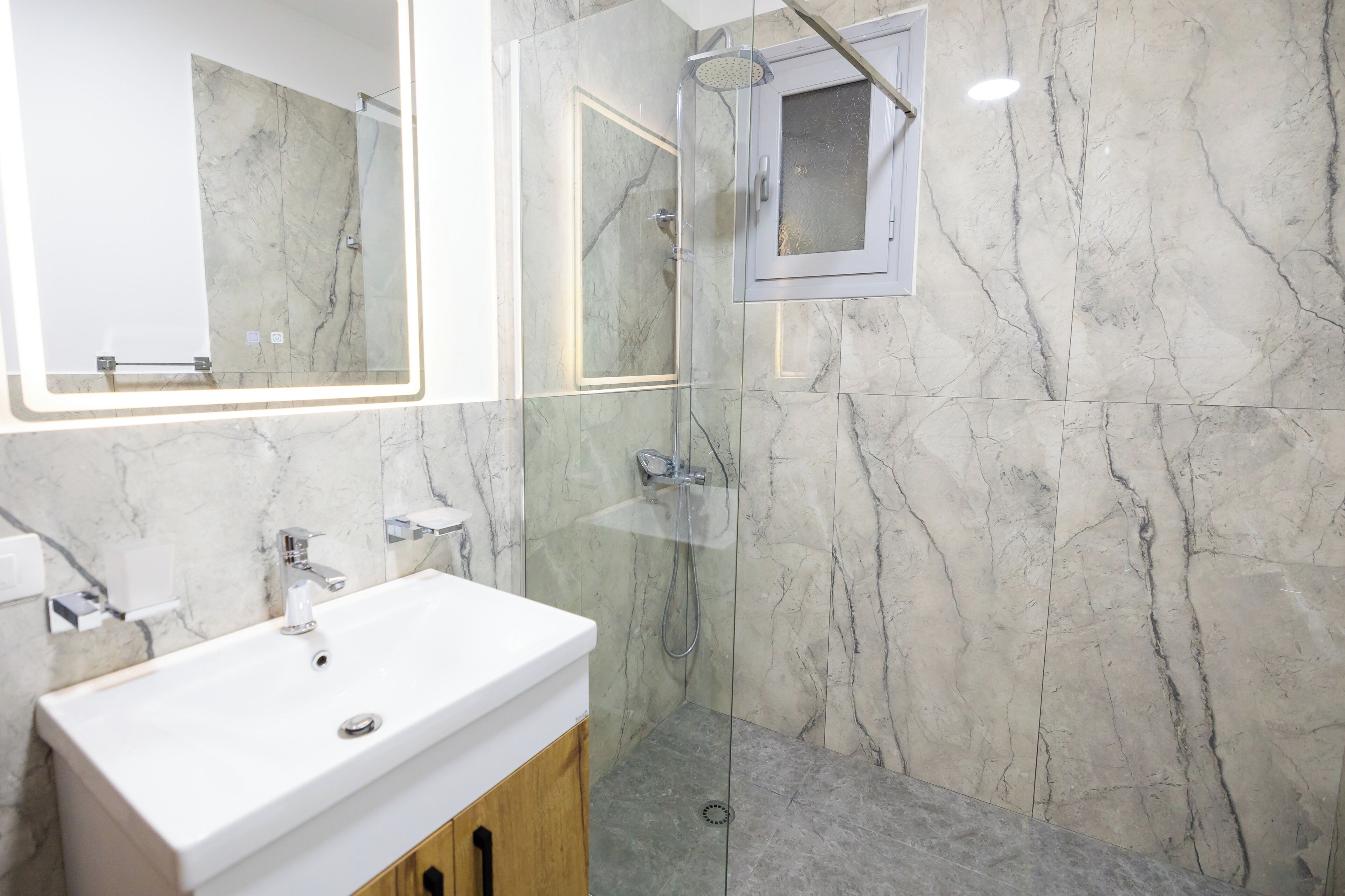 A bathroom with a white sink, a glass-enclosed shower, and marble walls.