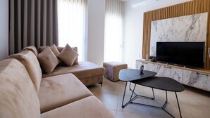 Una sala de estar moderna con sofá, otoman, televisor y una mesita.
