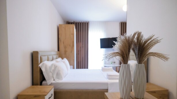 Una habitación de hotel moderna con una cama, mesitas de noche, un televisor y una mesita auxiliar de madera.