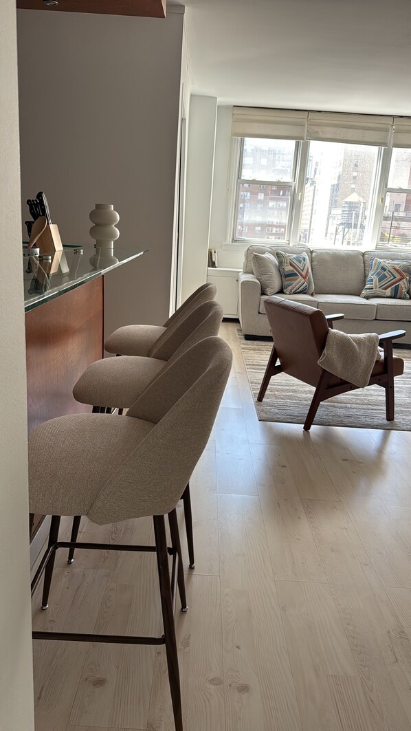 A modern living room with a sofa, two armchairs, a coffee table, and a dining area with chairs and a glass-top table.