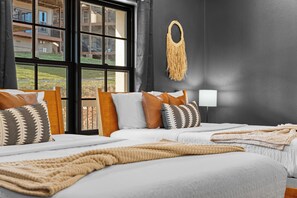 A hotel room with two beds, a large window, a macrame wall hanging, and a view of buildings outside. - Lake View~Hot Tub, Arcade, Pool, 1mi to SilverDC (Branson)