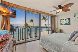 A bedroom with a balcony, a bed, a TV, and a ceiling fan. - KBM Resorts | FREE CAR | Valley Isle Resort | Oceanfront | 5th Floor 2-Bedroom Condo with Stunning views! VIR-508 (Lahaina)