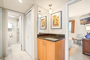 A modern bathroom with a shower, toilet, and vanity. There are two framed artworks on the wall, a ceiling light, and a TV mounted on the wall. - Valley Isle Villas | Oceanfront 2 BR | Car Incl. w/ 6+ Nights | VIR-508 by KBM (Lahaina)