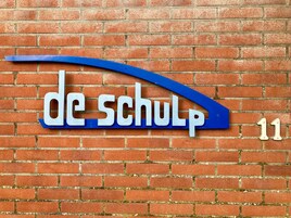 A brick wall with a blue and white sign that reads 'de school' and the number '11'.