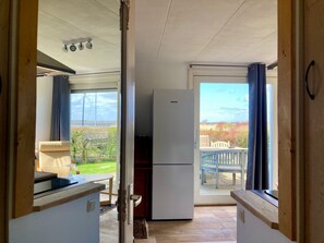 A compact kitchen with a refrigerator, a dining area with a table and chairs, and a view of the outdoors. - Unique Lakeside House With Sauna and Panoramic Harbour Views 5 Guests (Anjum)