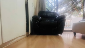 A room with a black leather chair, wooden flooring, a white wall, and a window with a view of trees. - 3 bed Cluster Home in Sandton (Johannesburg)