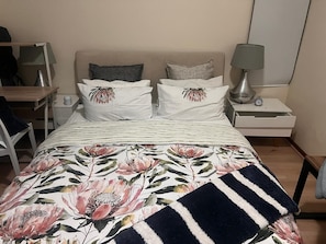 A bed with floral bedding, two pillows, a bedside table with a lamp, and a nightstand with a clock. - 3 bed Cluster Home in Sandton (Johannesburg)