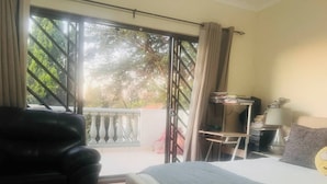 A bedroom with a bed, a chair, a desk, and a view through a large window. - 3 bed Cluster Home in Sandton (Johannesburg)