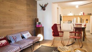 A living room with a striped sofa, a red rocking chair, a wooden wall, and a kitchen in the background. - Design Mountain Home in Center of Bormio (Bormio)