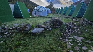 A series of green tents in a mountainous area with a clear sky and a snow-capped mountain in the background.