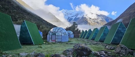 A series of green tents in a mountainous area with a clear sky and a snow-capped mountain in the background.