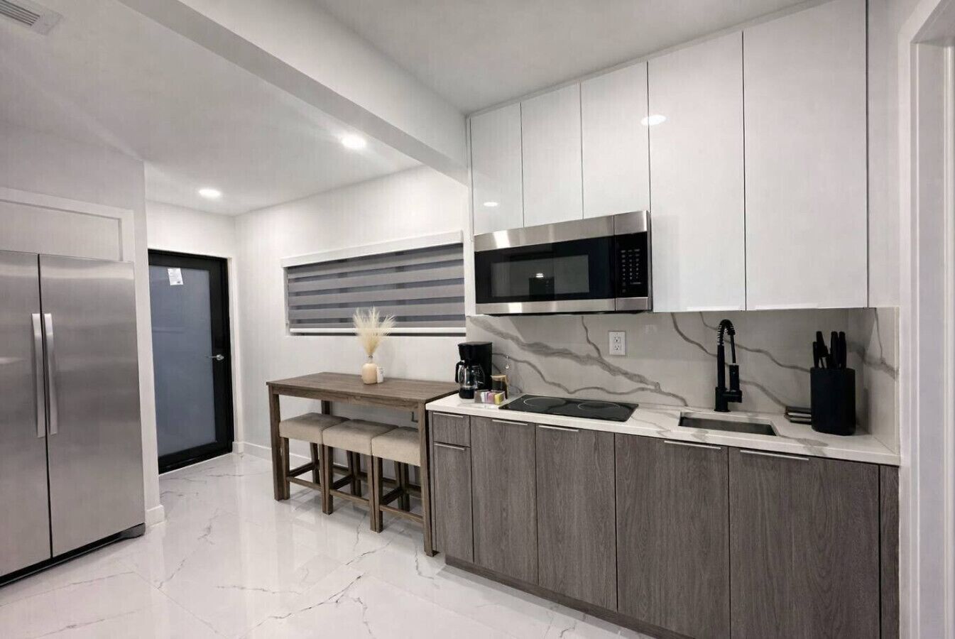 A modern kitchen with a built-in microwave, stainless steel refrigerator, and a marble backsplash.
