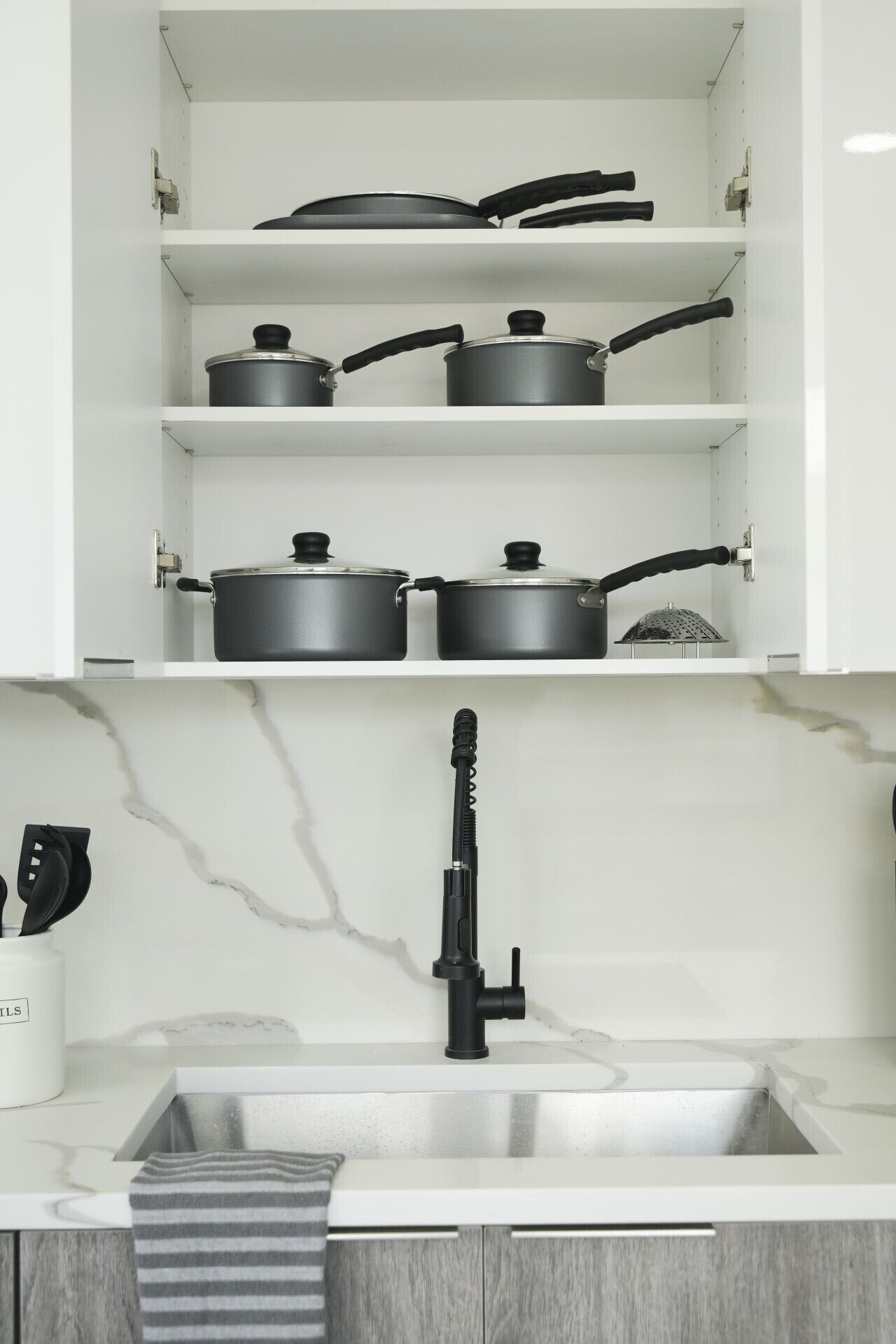 A kitchen with white cabinets, a stainless steel sink, and a marble backsplash.