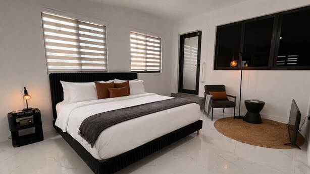 Une chambre à coucher moderne avec un grand lit, une table de chevet, une chaise, un tapis rond et un téléviseur.
