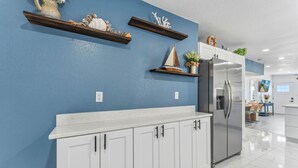 Una cucina con mobili bianchi, un frigorifero in acciaio inossidabile e oggetti decorativi sugli scaffali.