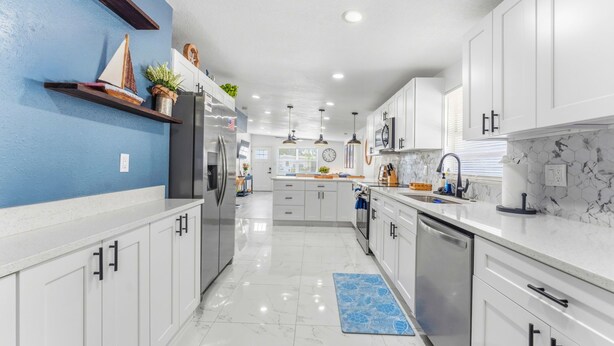 Una cucina moderna con mobili bianchi, una parete di colore blu e uno schienale in marmo.