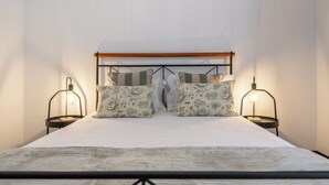 Een bed met een houten hoofdeinde, twee nachtkastjes met lampen, en kussens met een bloemenmotief.