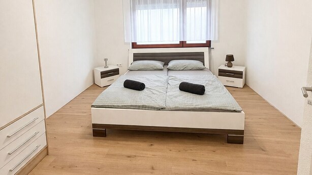 Een slaapkamer met een bed, nachtkastjes, een raam met gordijnen en een plafondventilator.