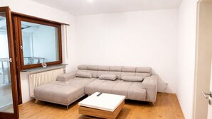 Een moderne woonkamer met een hoekbank, een houten salontafel en een glazen deur die uitkomt op een balkon.