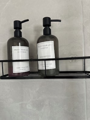 Two bottles of shampoo on a black shelf against a tiled wall.