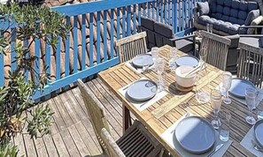 Eine Holzterrasse mit Esstisch, umgeben von Stühlen und einem blauen Zaun.