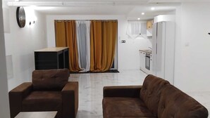A modern living room with a sofa, a coffee table, and a TV. There is a kitchen area with a refrigerator and a microwave.