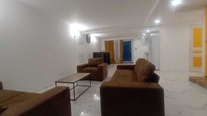 A living room with a sofa, armchair, and coffee table, a TV, and a door leading to a kitchen.