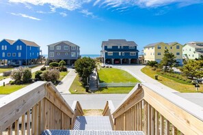 A residential area with a wooden deck, a clear sky, and houses with a uniform architectural style. - Sunny Hideaway | Oceanside | Walk to Beach | Deck (Emerald Isle)