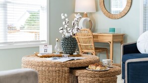 A cozy room with a wicker table, a lamp, a chair, and a view of the outside. - Sunny Hideaway | Oceanside | Walk to Beach | Deck (Emerald Isle)
