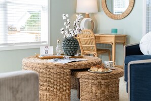 A cozy room with a wicker table, a lamp, a chair, and a view of the outside. - Sunny Hideaway | Oceanside | Walk to Beach | Deck (Emerald Isle)