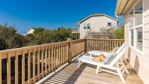 A wooden deck with white lounge chairs and a small table, overlooking a residential area with houses and greenery. - Sunny Hideaway | Oceanside | Walk to Beach | Deck (Emerald Isle)