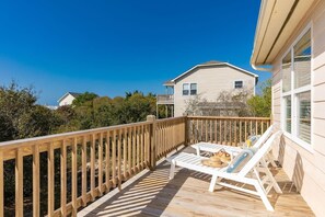 A wooden deck with white lounge chairs and a small table, overlooking a residential area with houses and greenery. - Sunny Hideaway | Oceanside | Walk to Beach | Deck (Emerald Isle)
