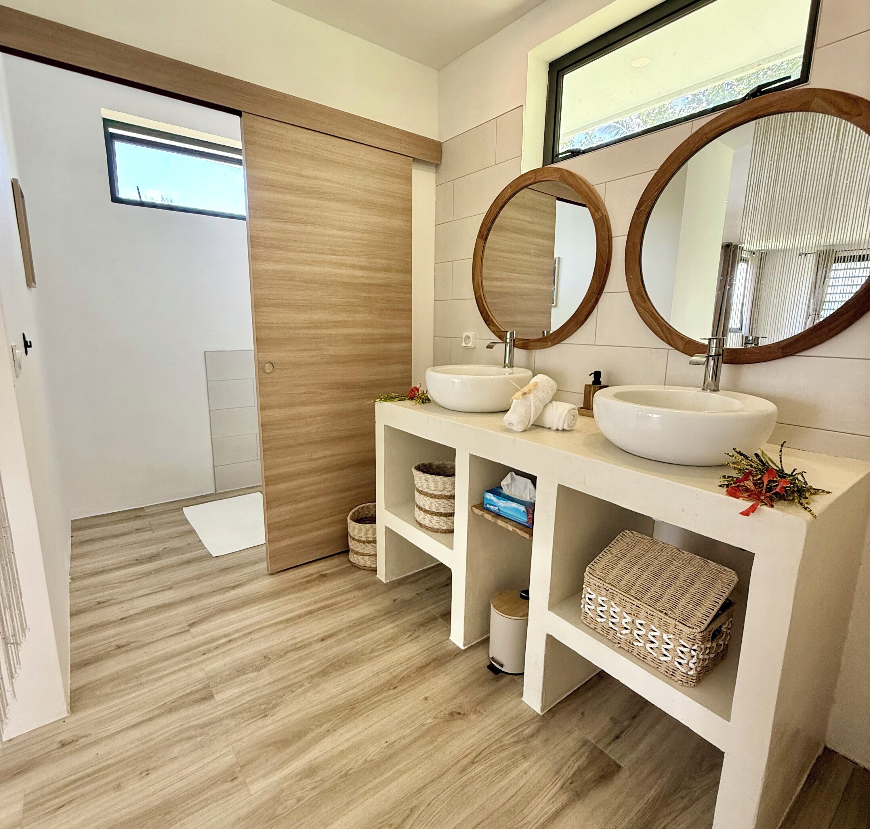 A modern bathroom with two sinks, wooden flooring, and a large mirror.