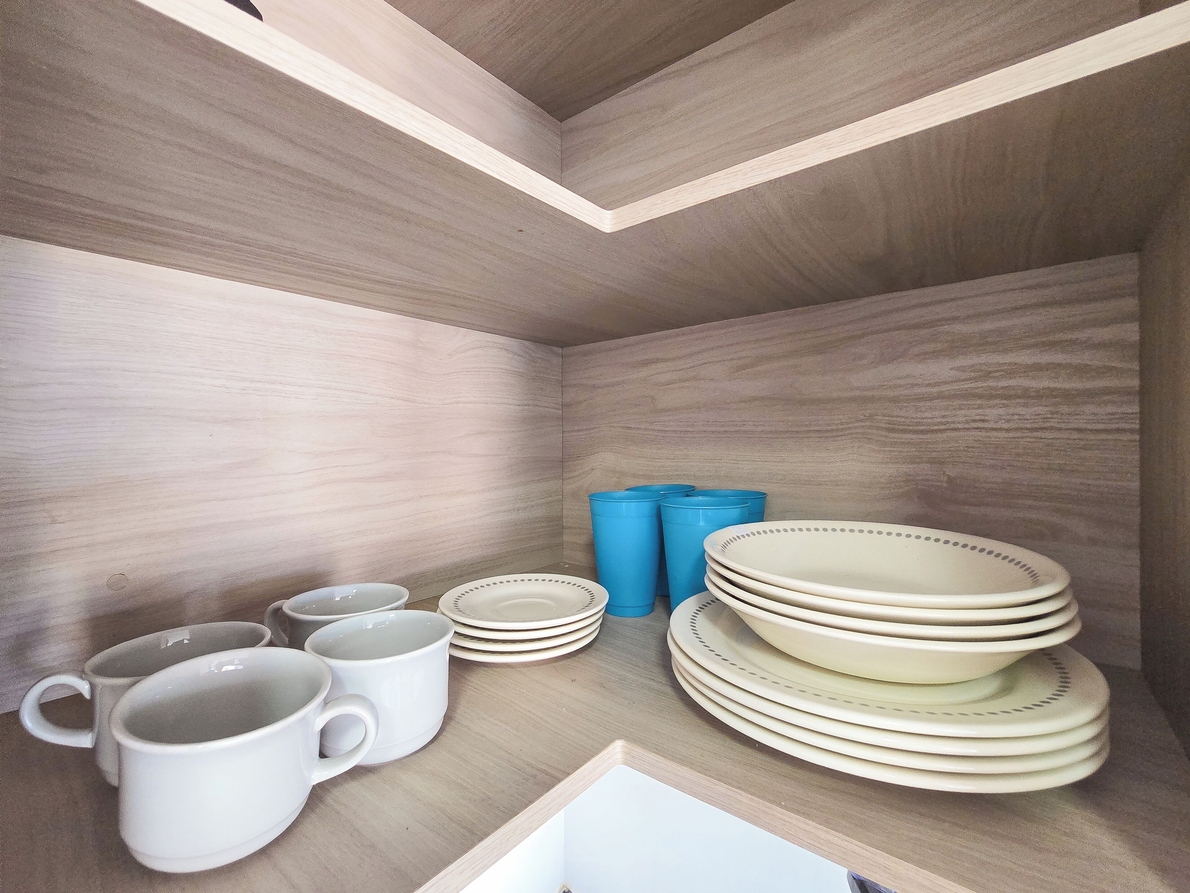 Un espace de rangement avec des étagères où sont entreposées des tasses blanches, des assiettes et des récipients bleus.