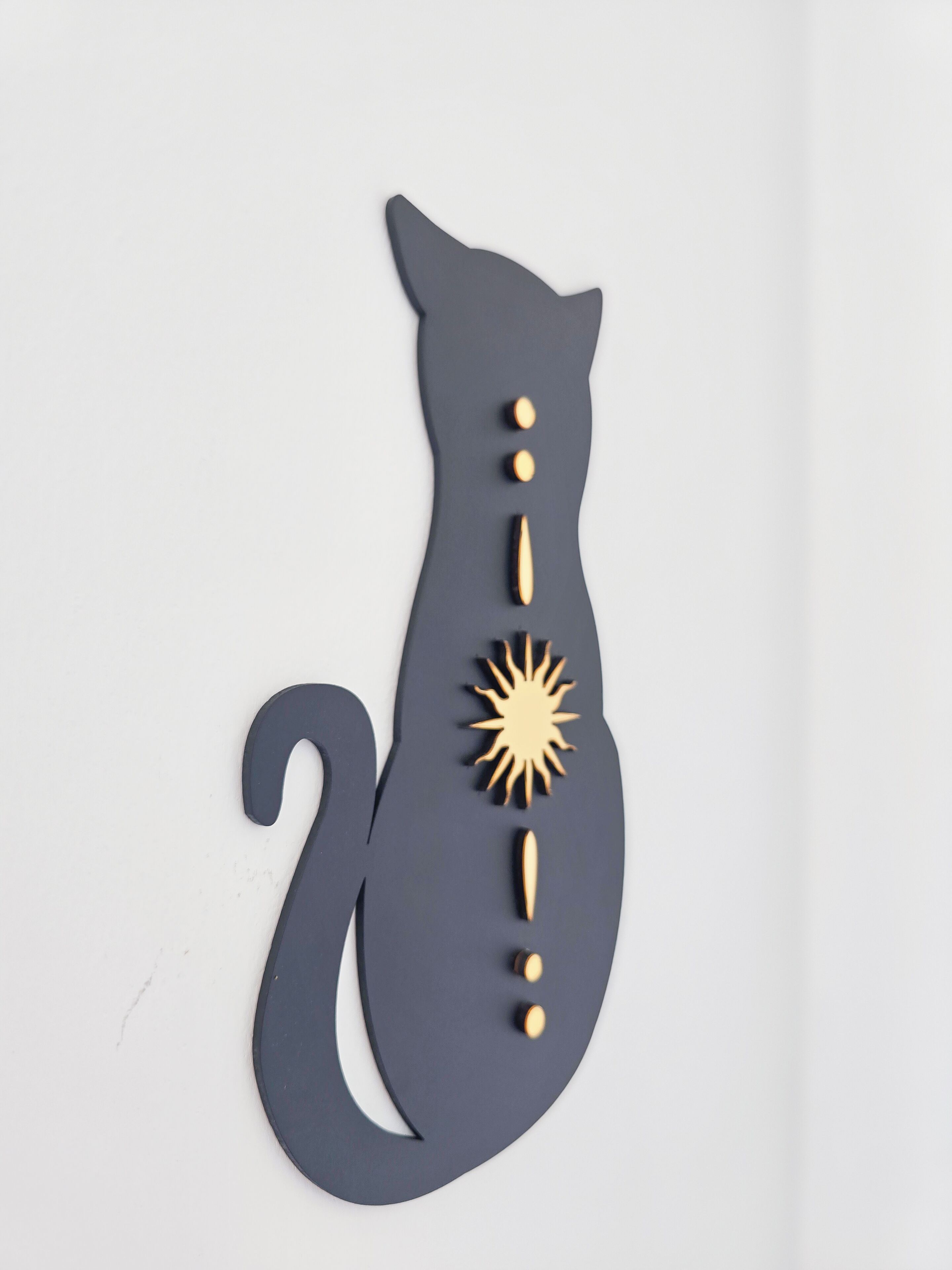 Een aan de muur bevestigde kat decoratie met een staart, een zonnestraal en drie knopen.