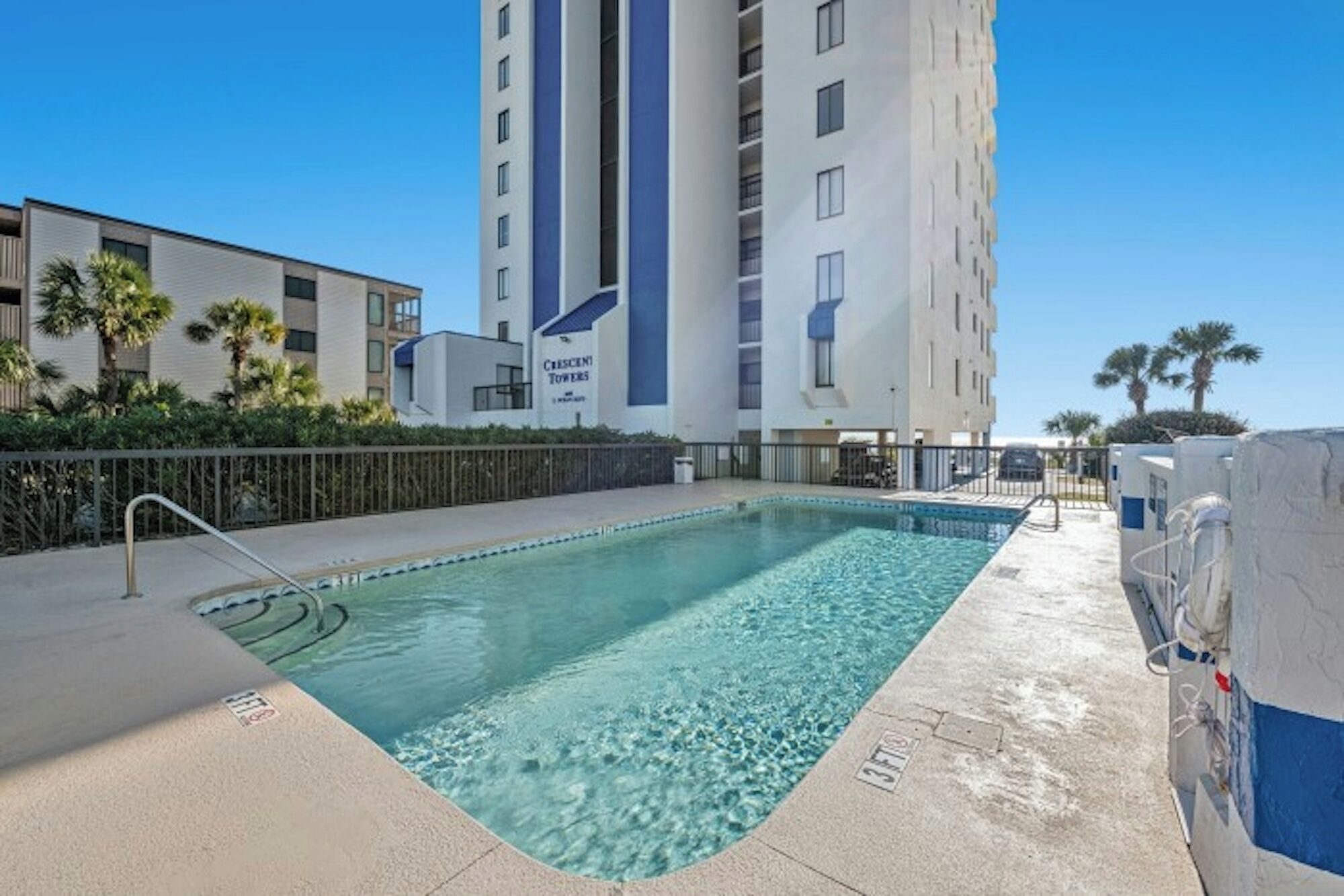 A swimming pool with a pool ladder, a lifeguard chair, and a poolside area with a fence.