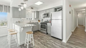 A modern kitchen with a central island, stainless steel appliances, and a view through the window. - Oceanfront Corner Unit-Crescent Towers I 804-Pool (North Myrtle Beach)