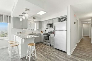 A modern kitchen with a central island, stainless steel appliances, and a view through the window. - Oceanfront Corner Unit-Crescent Towers I 804-Pool (North Myrtle Beach)