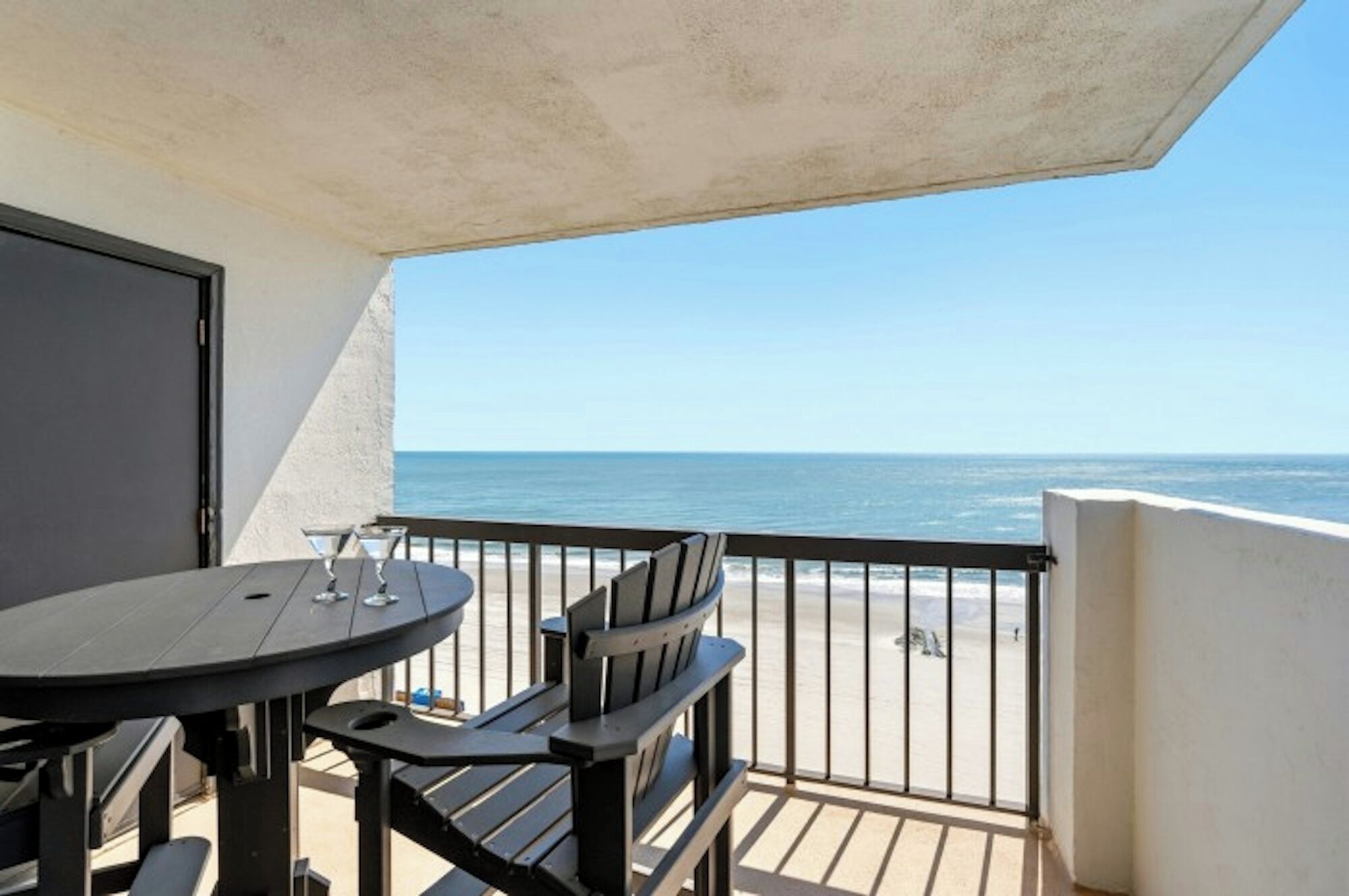 A balcony with a table and chairs, overlooking a beach.