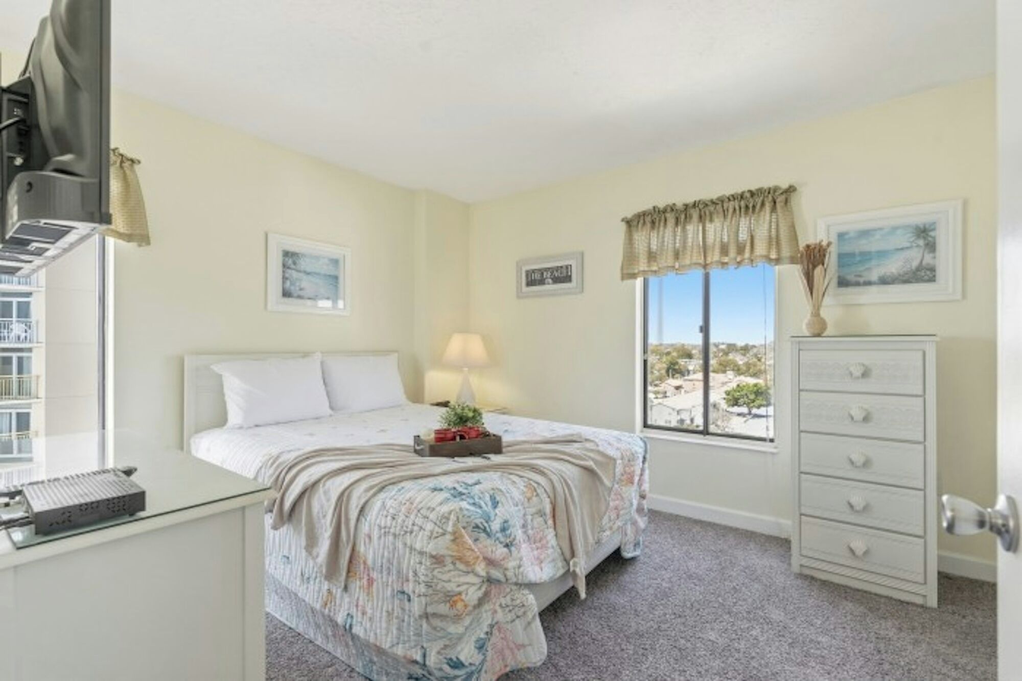 A bedroom with a bed, a desk, a dresser, and a window with a view.