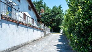 Ein gepflasterter Weg, der von einem weißen Gebäude mit Metallgitter und einer Steinmauer begleitet wird.
