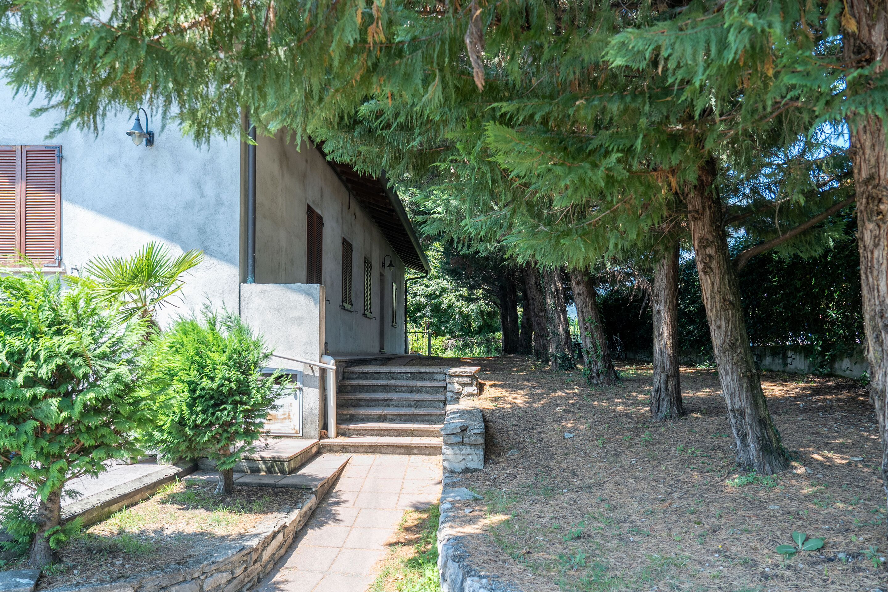 Un edificio con una escalera de piedra que lleva a una puerta, rodeado de árboles y un muro de piedra.