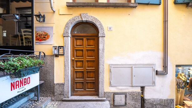 Une entrée d’immeuble avec une porte en bois, une enseigne indiquant « NANDO » et une fenêtre donnant sur la rue.