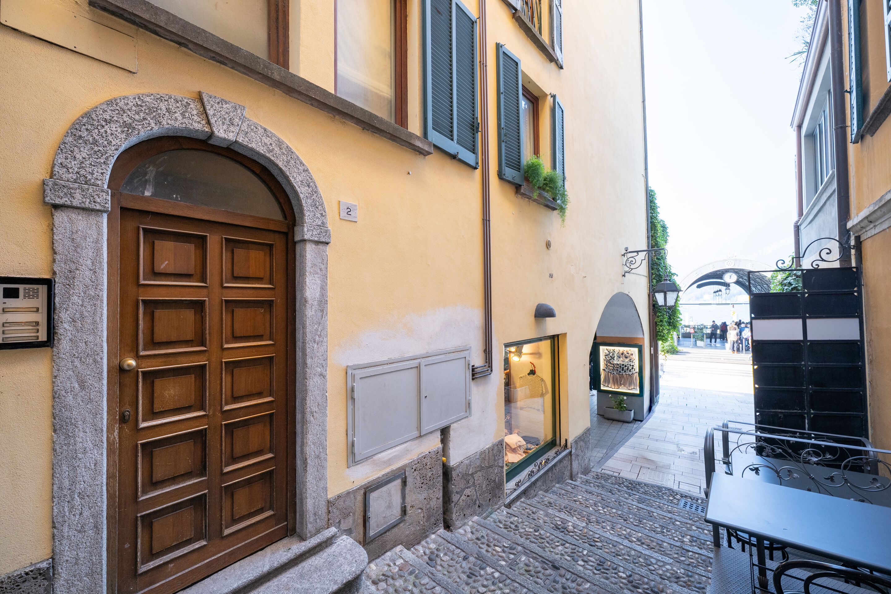 A narrow street with a stone archway leading to a building with a wooden door and shutters.