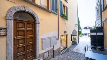 A narrow street with a stone archway leading to a building with a wooden door and shutters.